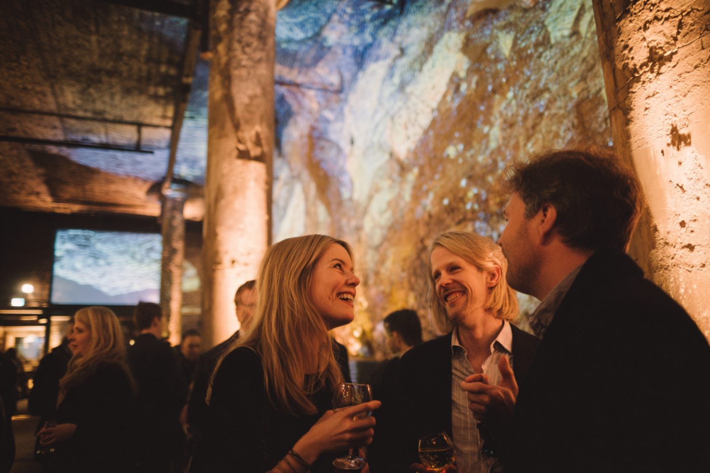 Invités en train de rire dans une halle industrielle habillée de projections
